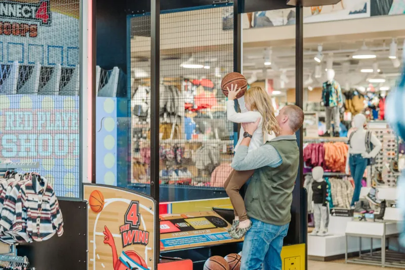 Adult lifting a child to shoot a basketball at an arcade game in a retail store