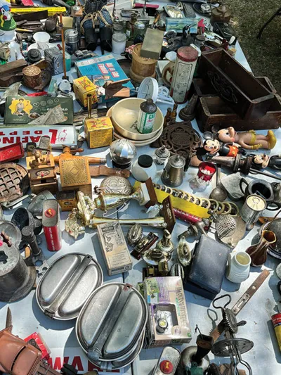 Cluttered flea market table covered with vintage tins, figurines, lamps, and assorted antiques