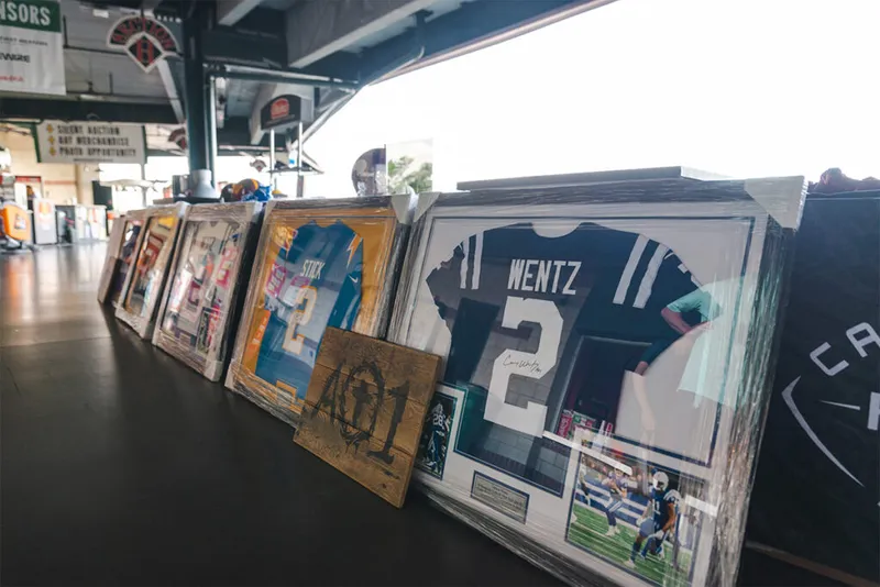 Framed sports jerseys including a signed Wentz No. 2 jersey lined up on a table at a charity event