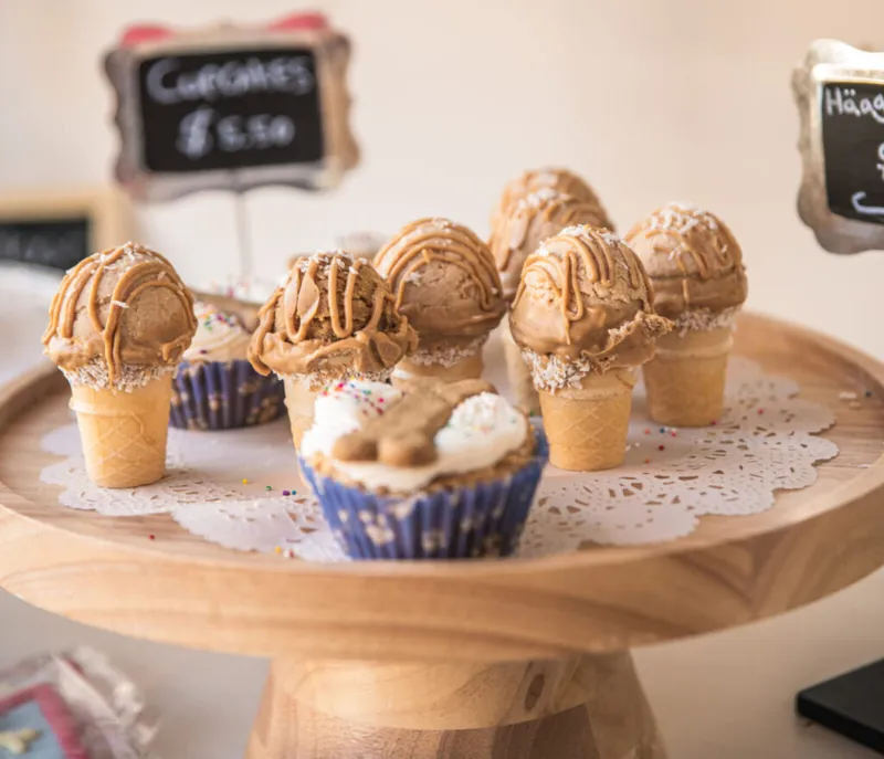 Ice cream cone cupcakes with caramel frosting on a wooden cake stand, with a chalkboard price sign behind