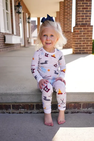 Smiling toddler girl in printed pajamas sitting on brick porch steps