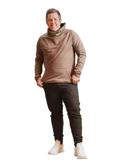 Smiling middle-aged man in a tan hoodie, dark joggers, and white sneakers