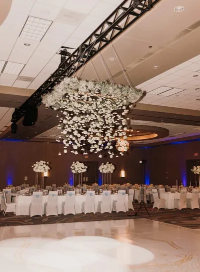 Ballroom reception with white floral chandelier, draped tables, and blue uplighting