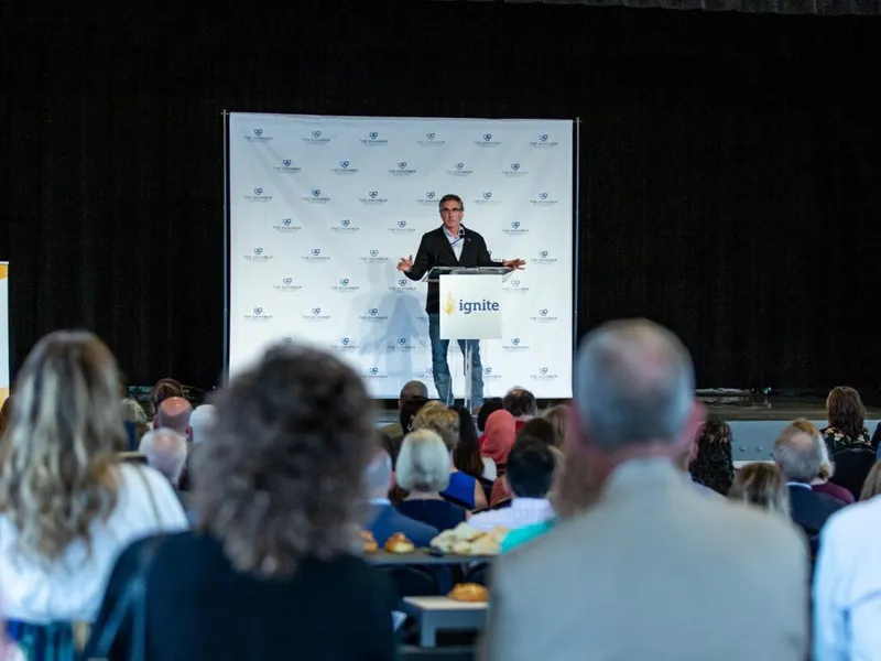 Man speaking at an Ignite-branded podium before a seated audience at an indoor event
