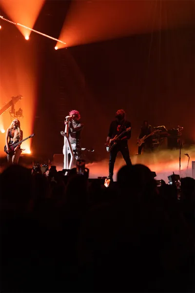 Rock band performs on a smoke-filled stage bathed in orange light before a packed crowd