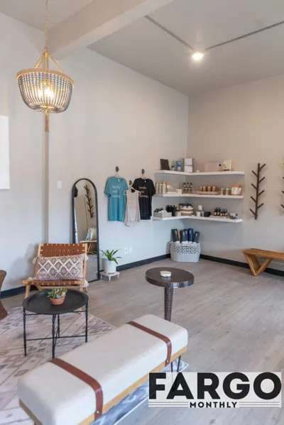 Bright boutique studio interior with pendant light, woven chair, shelved products, and hanging shirts