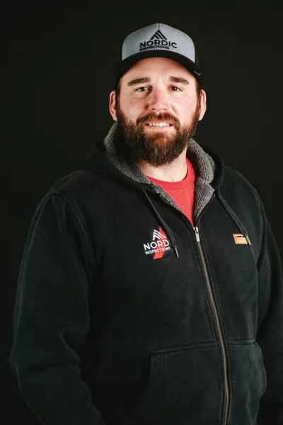 Bearded man smiling in a black Nordic Inspections hoodie and branded cap