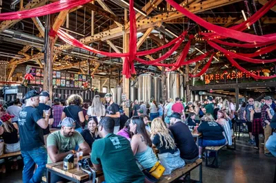 Crowded brewery taproom with red draped ceiling and string lights during a festival