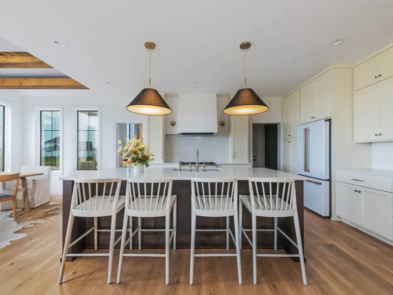 Modern farmhouse kitchen with dark island, white bar stools, and two black pendant lights