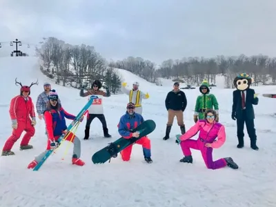 Group of skiers in colorful retro costumes and mascot suits posing on a snowy ski hill