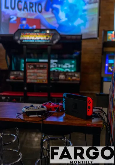 Nintendo Switch and two wired controllers on a bar table with arcade cabinets in the background