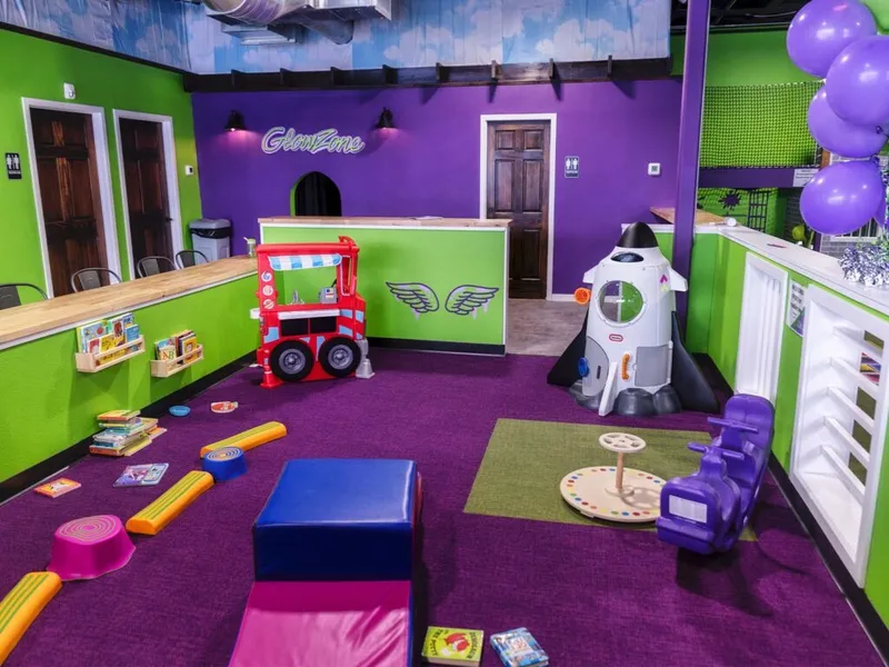 Bright green and purple children's play area with a toy rocket, play truck, foam blocks, and a GlowZone reception desk