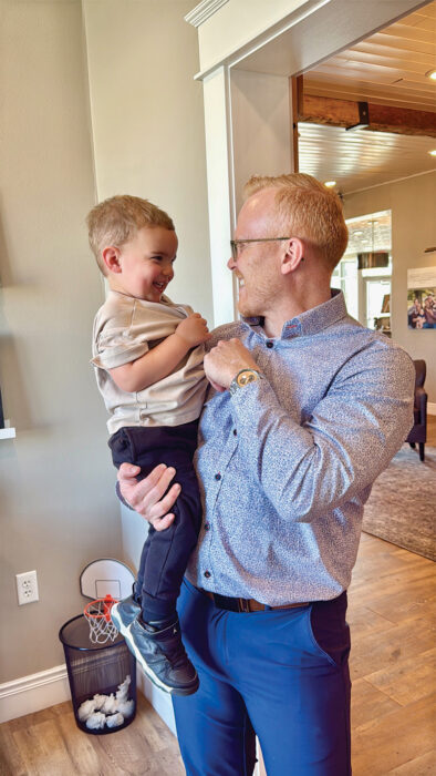 Man in blue patterned shirt holding a laughing toddler indoors
