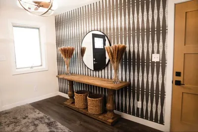 Entryway with bold geometric wallpaper, wood console table, round mirror, and dried grass arrangements