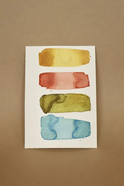 Four horizontal watercolor swatches in gold, red, olive, and blue on white paper
