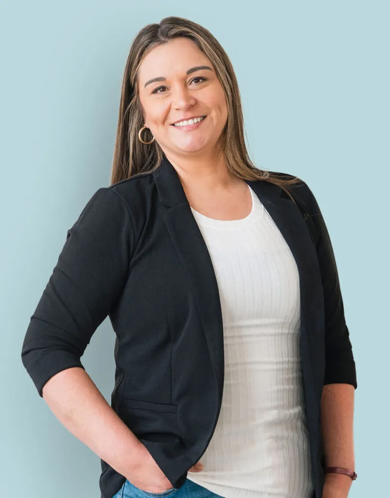 Smiling woman with long brown hair in a black blazer and white top against a light blue background