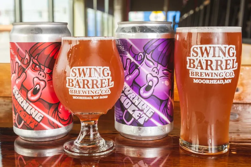 Two Swing Barrel Brewing Co. poured glasses flanked by red and purple beer cans on a bar top