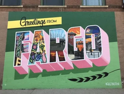Colorful "Greetings From Fargo" mural on a brick building with city scenes inside each letter