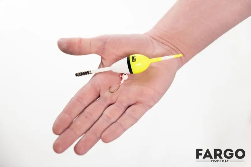 Open palm holding a small yellow and white fishing bobber with a hook