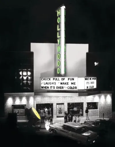 Hollywood theater marquee lit at night with vintage cars parked out front