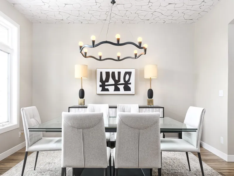 Modern dining room with glass-top table, gray upholstered chairs, wavy black chandelier, and patterned ceiling