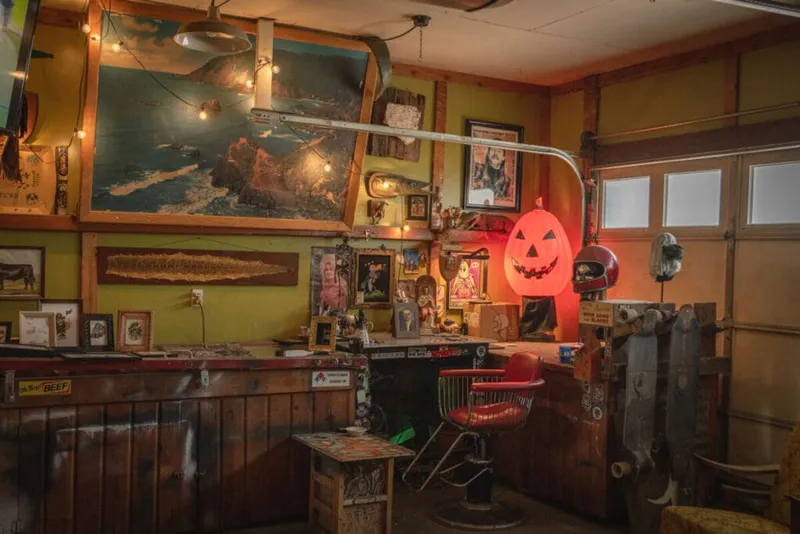 Eclectic studio interior with a glowing jack-o'-lantern, barber chair, and wall art under string lights