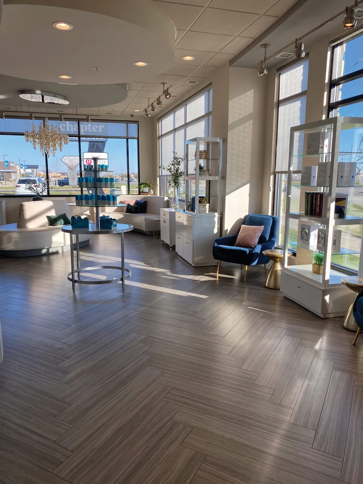 Bright modern spa lobby with herringbone tile floors, a blue velvet chair, white curved seating, and floor-to-ceiling windows