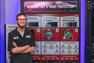 Smiling technician with crossed arms standing before a window tint and paint protection display
