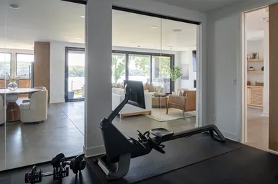Home gym with rowing machine on dark mat opening to bright modern living area