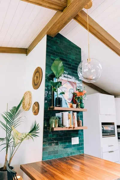 Vaulted kitchen with dark green tile accent wall, floating wood shelves, and globe pendant light