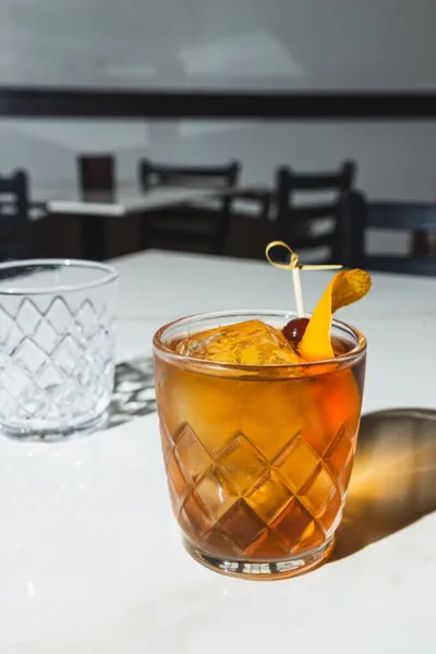 Amber cocktail with cherry and orange peel garnish in a cut-crystal rocks glass
