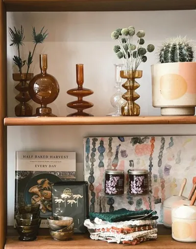 Styled wooden shelves with amber glass vases, dried florals, a cactus, and a cookbook