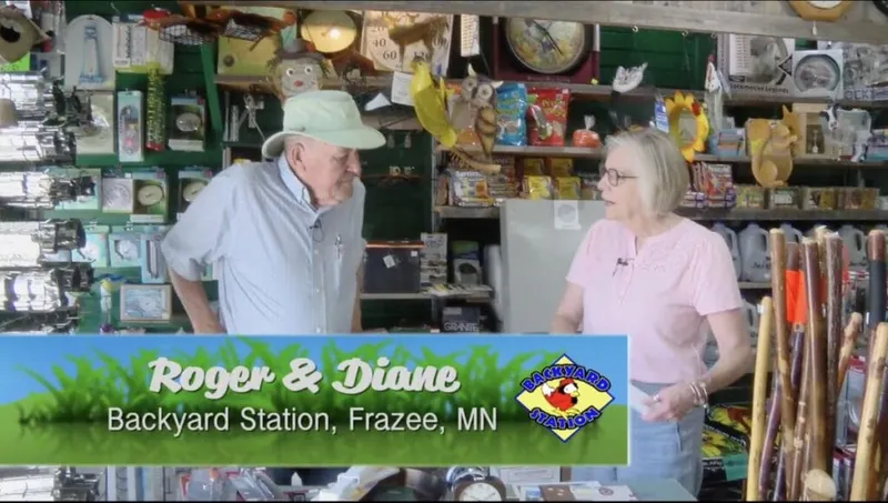 Two people conversing inside a cluttered gift shop, on-screen text reads Roger & Diane, Backyard Station, Frazee MN