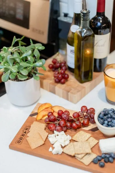 Charcuterie board with grapes, crackers, cheese, blueberries, and peach slices beside two wine bottles