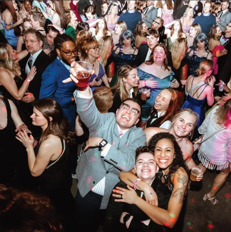 Crowd of smiling dressed-up guests dancing at a lively indoor party