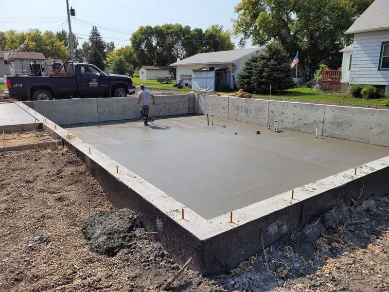 Worker smoothing freshly poured concrete foundation slab at a residential construction site