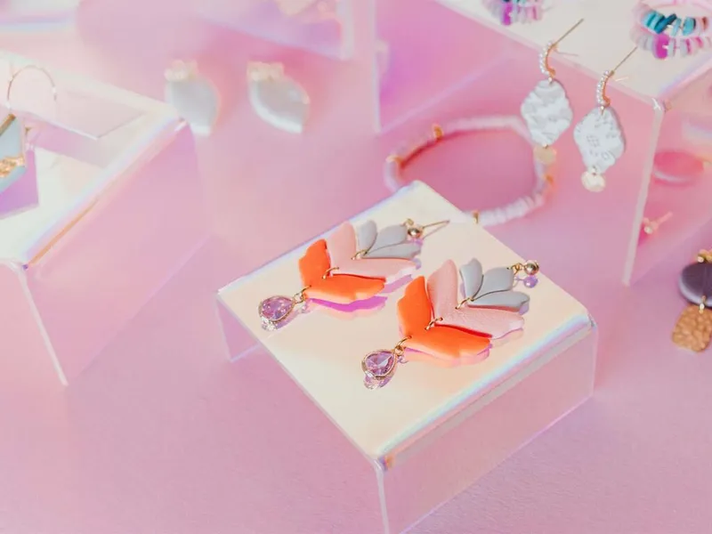 Colorful geometric drop earrings with lavender crystal pendants displayed on a pink acrylic jewelry stand