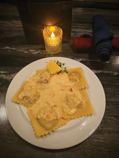 Ravioli topped with grated cheese and a lemon wedge on a white plate beside a lit candle