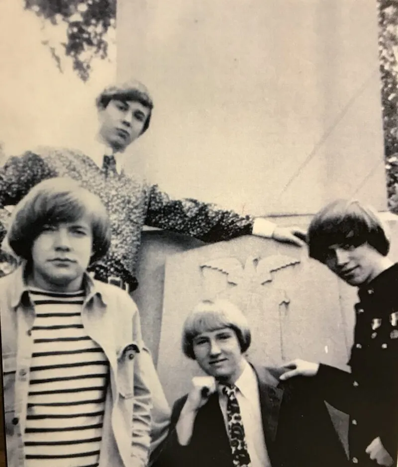 Four young men with mod haircuts posing near a stone monument in a black-and-white 1960s photo