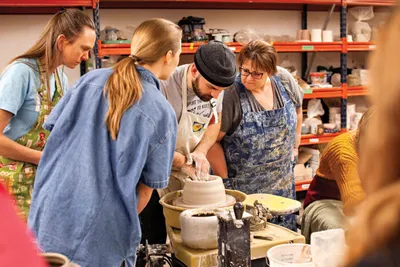 Group of adults gathered around a pottery wheel during a clay workshop