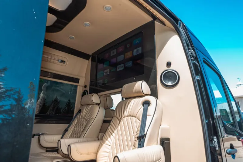 Cream quilted leather captain's chairs and a wall-mounted TV inside a luxury custom van