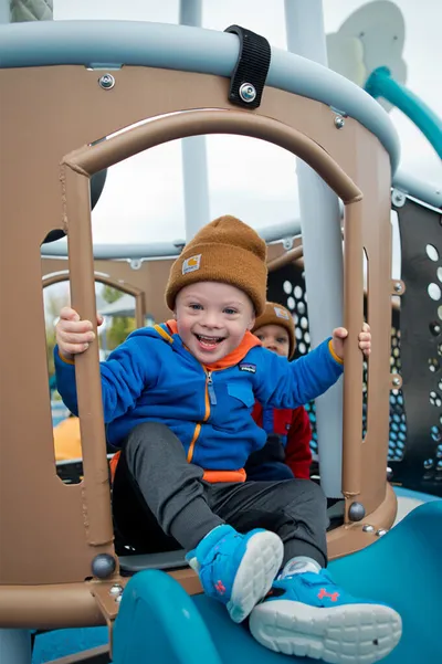 Smiling young child in a blue hoodie and tan beanie on a playground structure