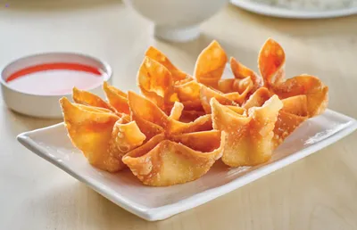 Golden fried wontons on a white plate with red dipping sauce