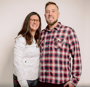 Two smiling adults posed together against a light gray background
