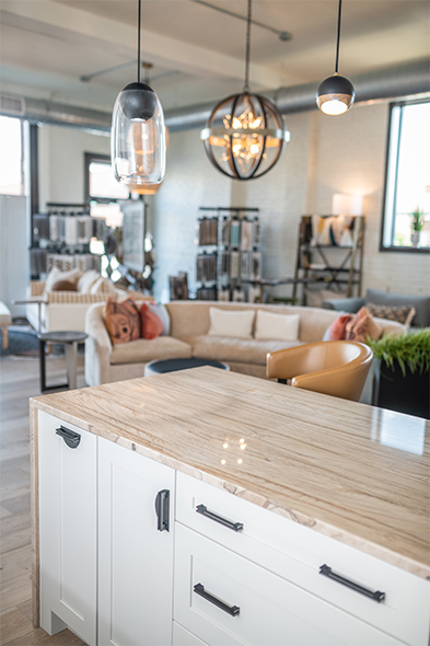 White kitchen island with marble countertop beneath pendant lights in an open design studio showroom