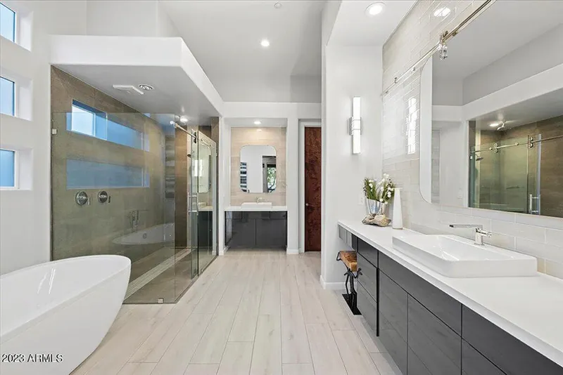 Modern primary bathroom with freestanding soaking tub, glass-enclosed shower, and dark floating double vanity
