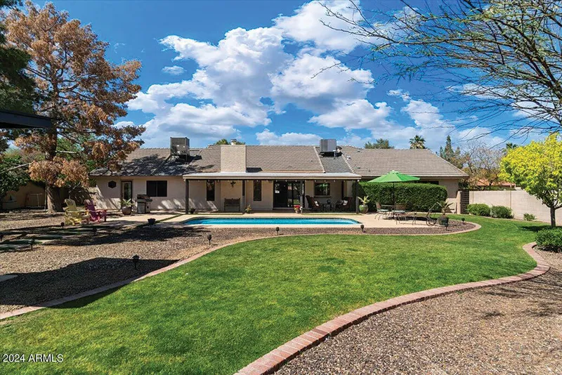 Single-story ranch home with backyard pool, green lawn, and patio under blue sky