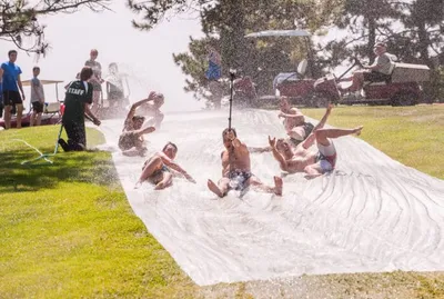 Kids sliding down a wet tarp slip-and-slide on a grassy lawn in summer sunshine