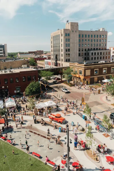 Aerial view of a busy downtown plaza with crowds, white tents, and a vintage red car on a sunny day