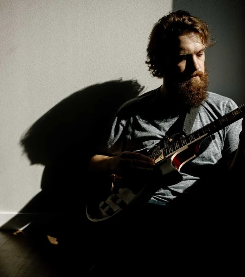 Bearded man with curly hair playing an electric guitar in dramatic shadow lighting